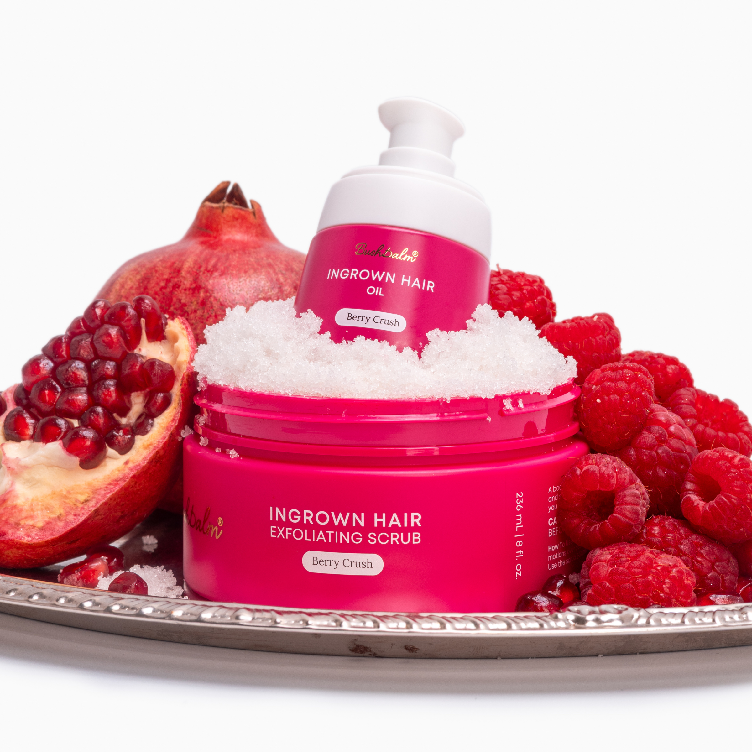 Pink containers of ingrown hair products on a tray with raspberries and half a pomegranate.