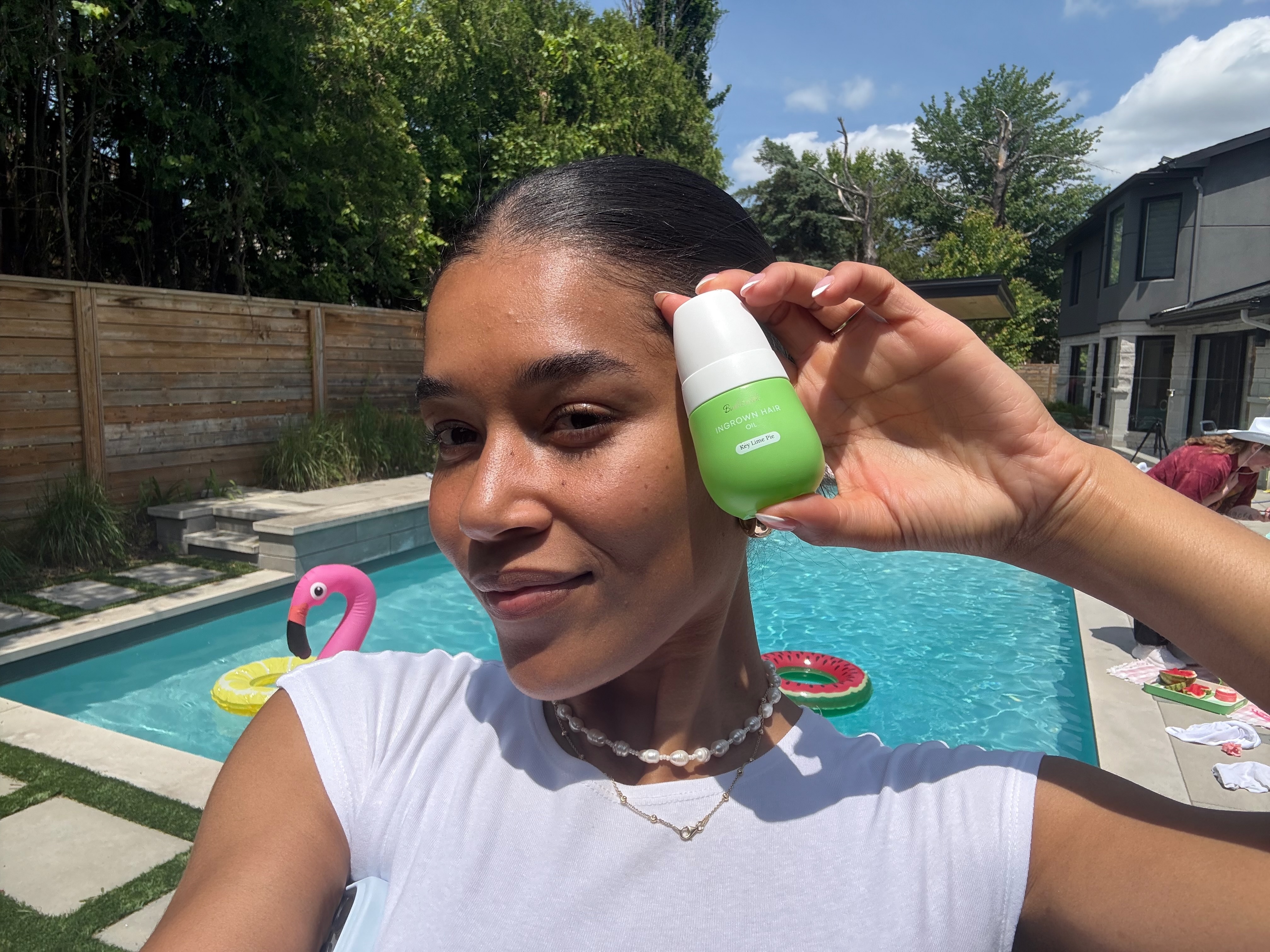 Person holding a green bottle by a pool with inflatable toys.