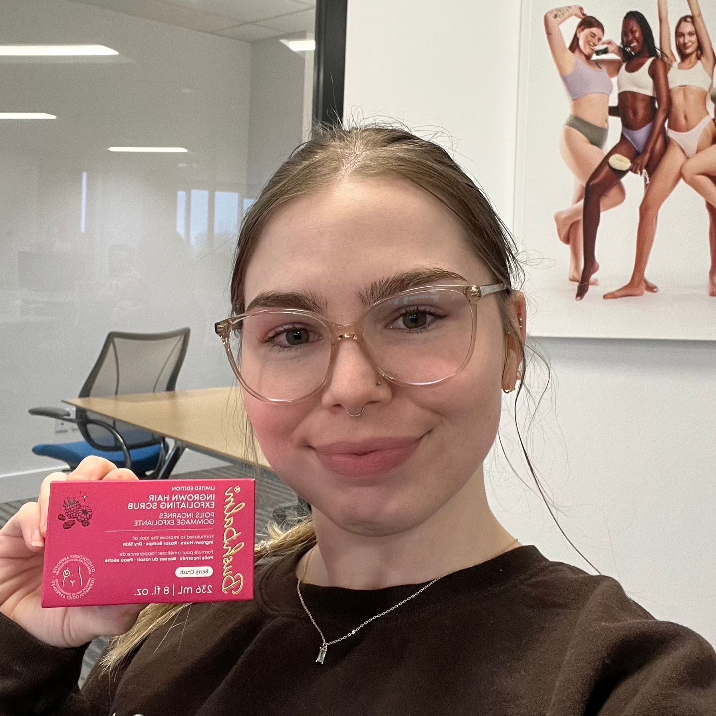 Person holding a skincare product box, with a poster of diverse models in the background.
