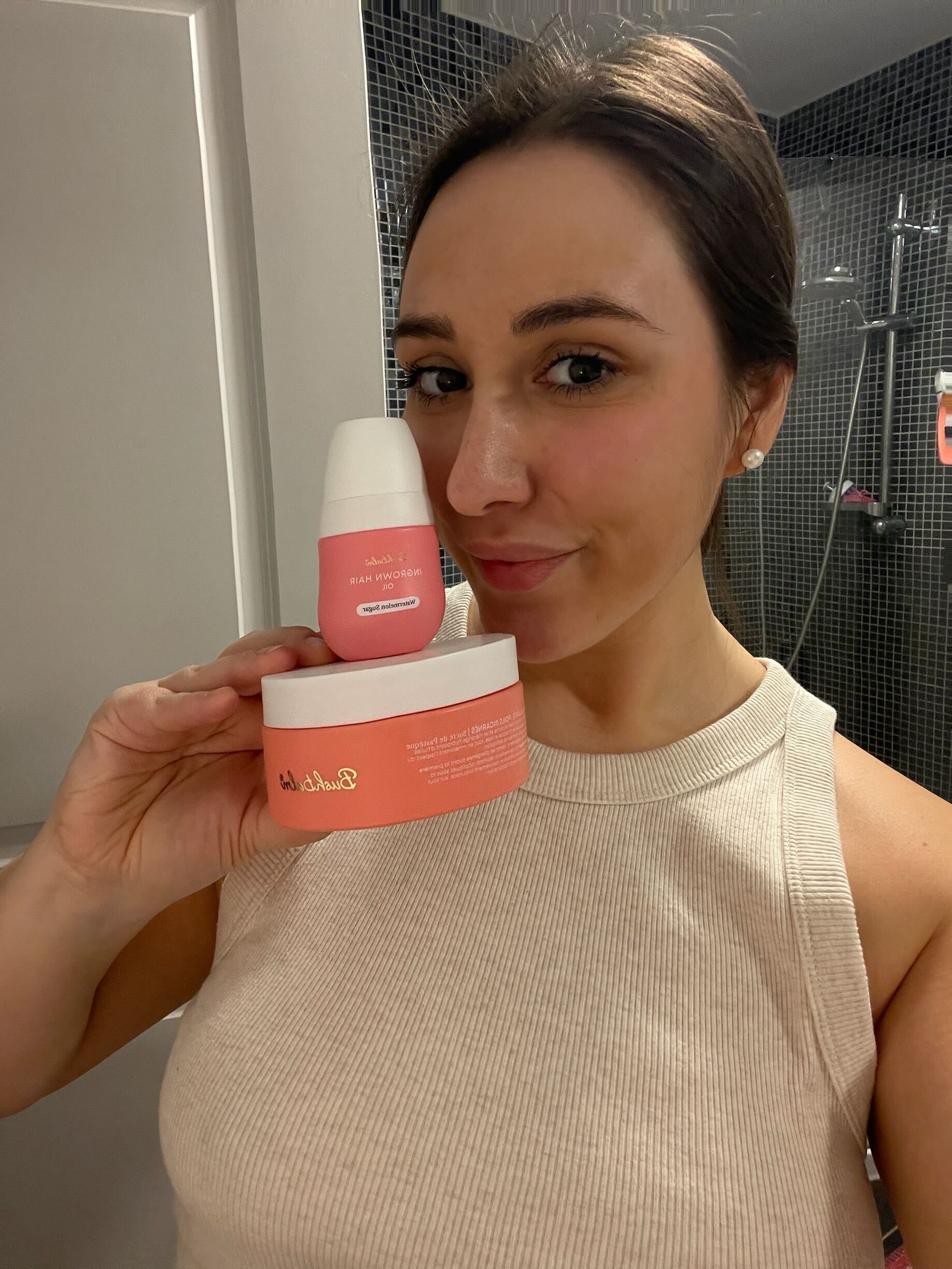 Person holding two pink skincare products in a bathroom.