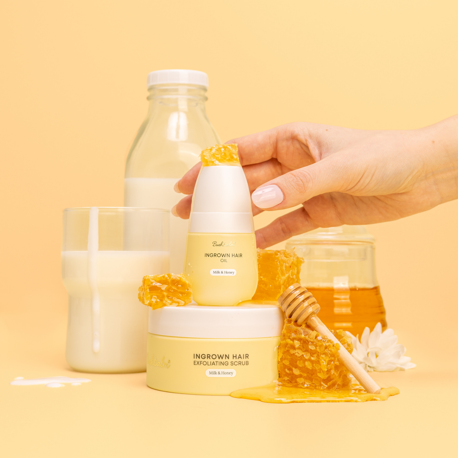 A still life of milk and honey hair products, with a hand, honeycomb, and a glass of milk.