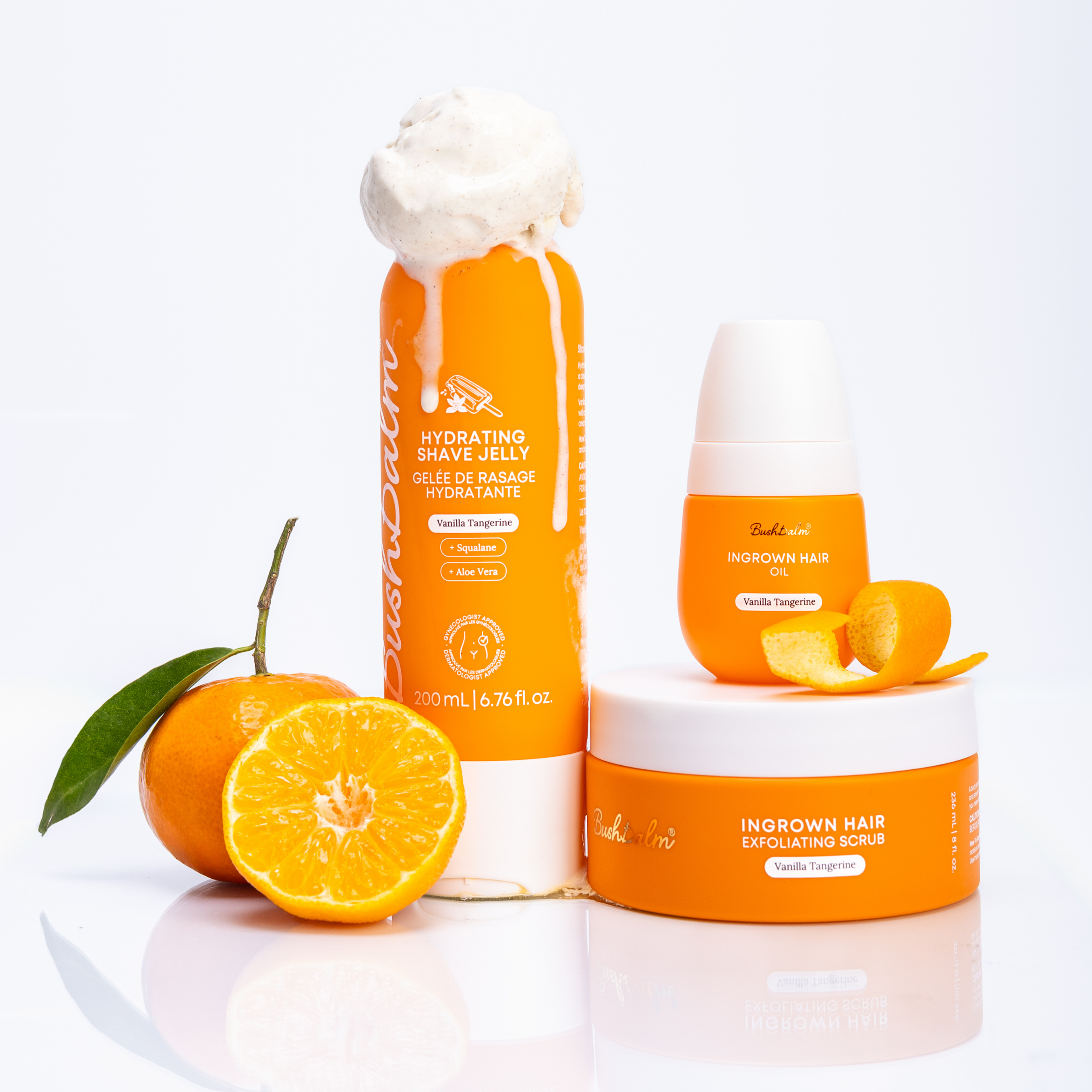 Bushbalm Vanilla Tangerine shave jelly, ingrown hair oil, and scrub displayed with fresh tangerines on white.