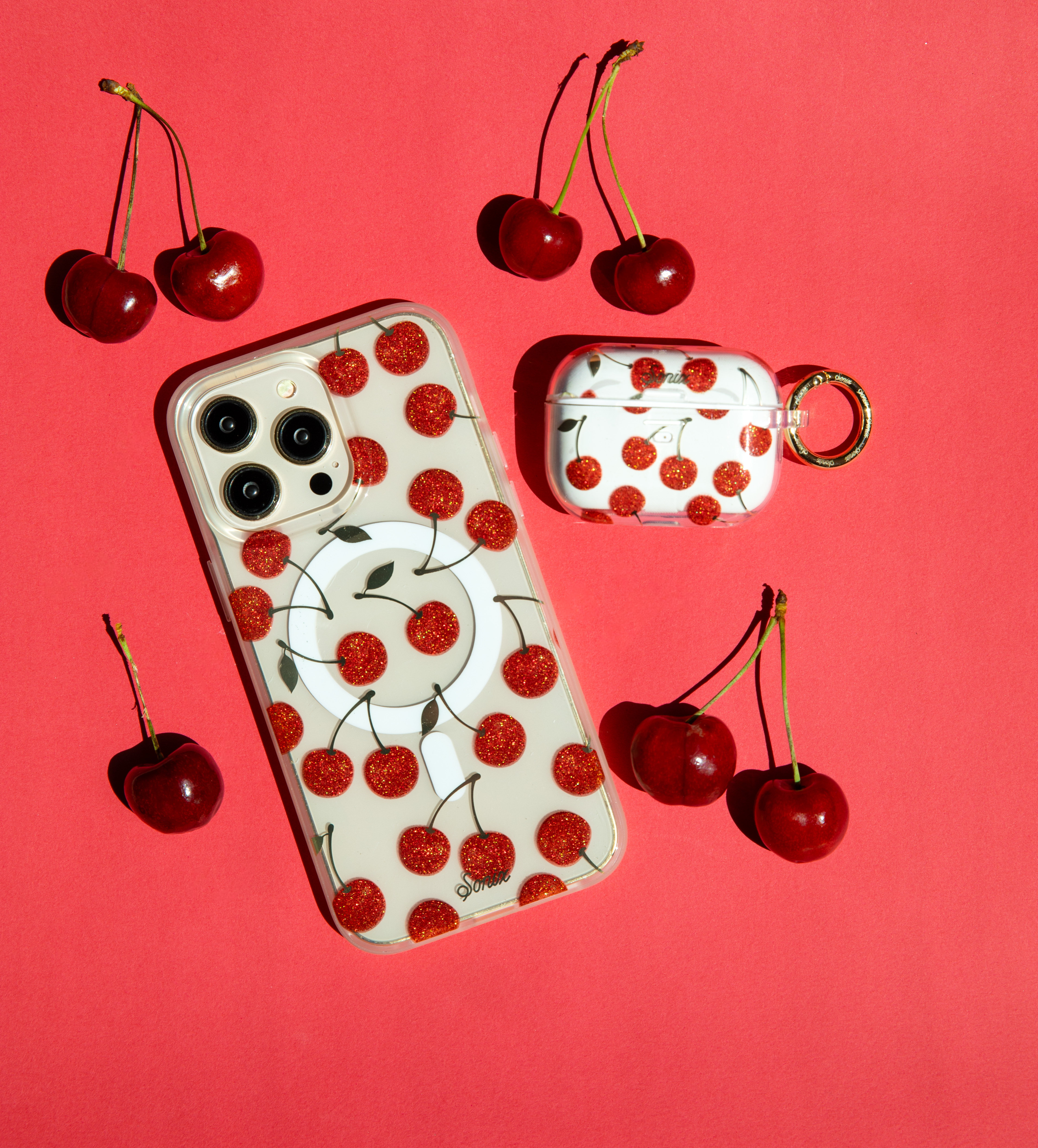 Phone and AirPods case with cherry design on red background.
