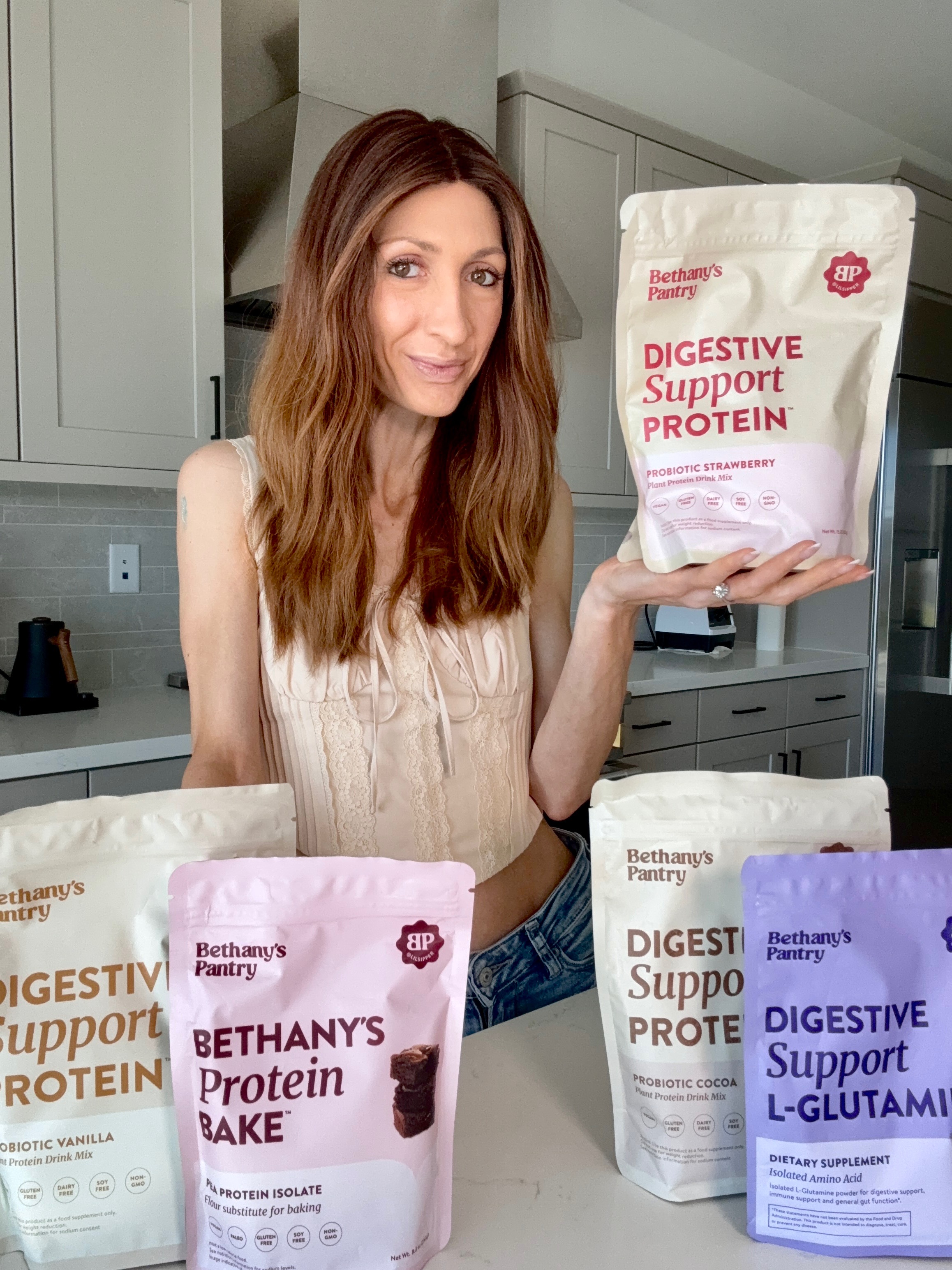 Person holding a Digestive Support Protein bag in a kitchen with similar products displayed.