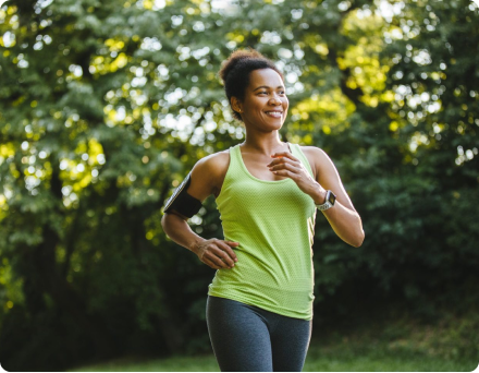 Person jogging in a park, wearing a green tank top and fitness tracker.