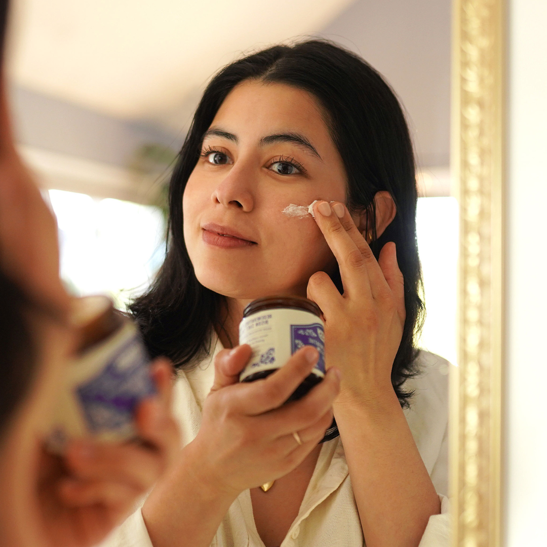 Person applying cream to their face in front of a mirror.