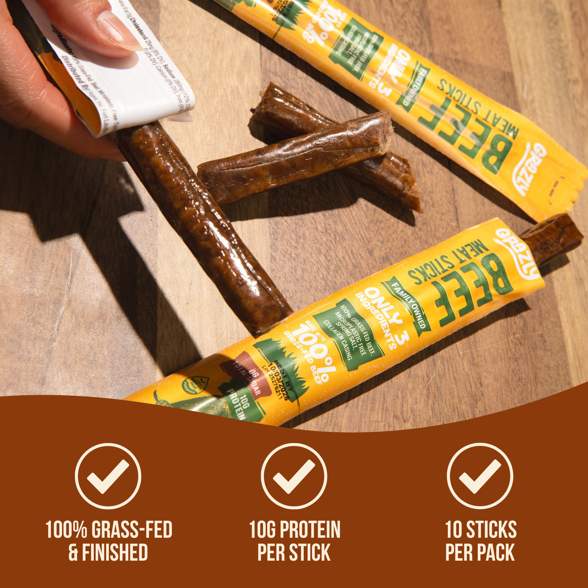 Person opening a beef meat stick package on a wooden surface.