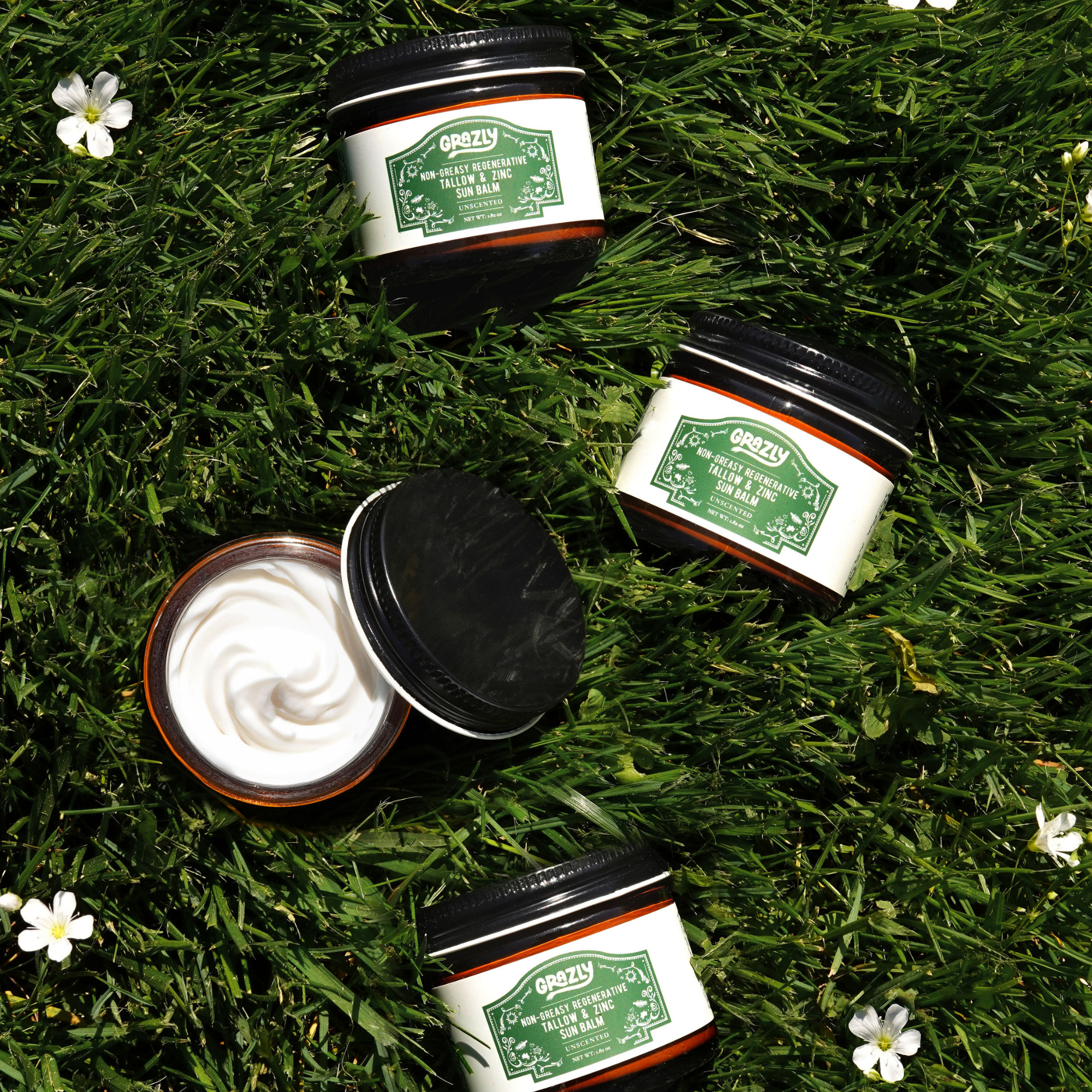 Four jars of cream on grass with small white flowers.