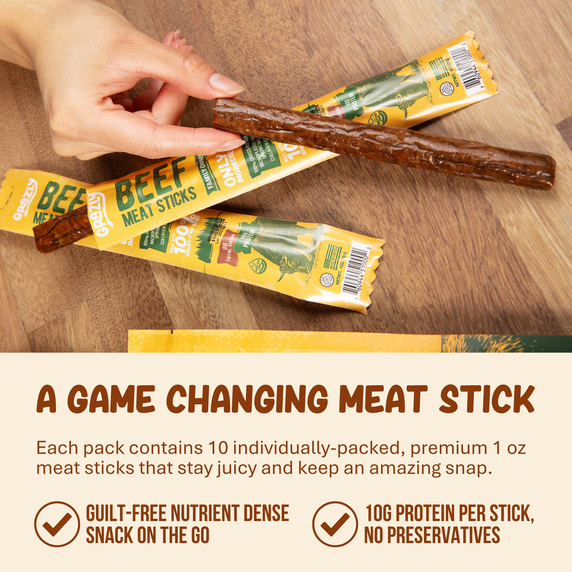 Person holding a beef meat stick above two wrapped packages on a wooden surface.
