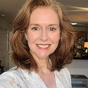 A person smiling indoors with a kitchen in the background.