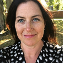 Woman with dark hair and polka dot shirt smiling outdoors.