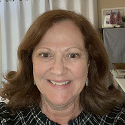 A woman smiling indoors with a curtain and framed pictures in the background.