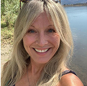 Person smiling by a river with trees in the background.