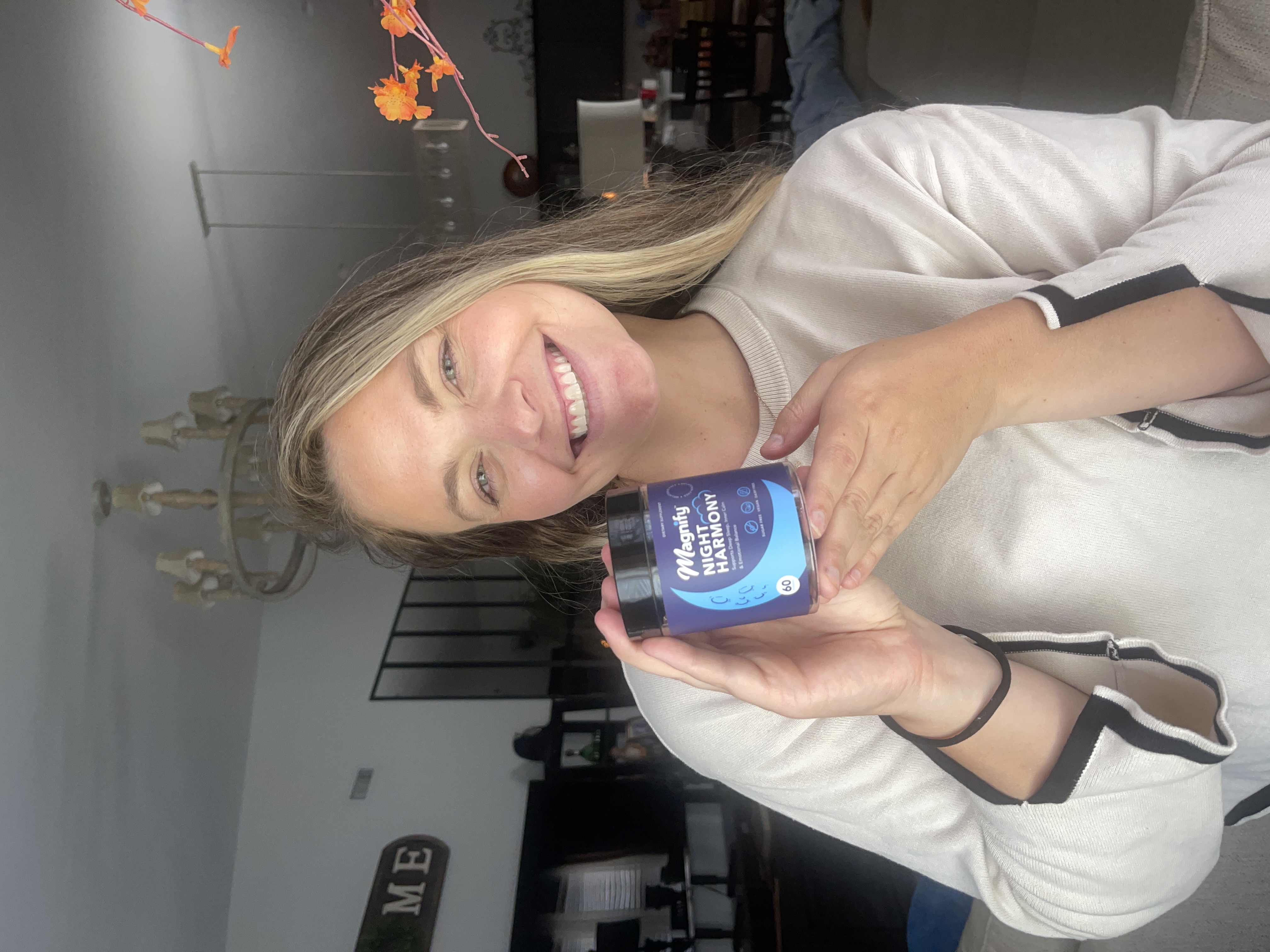 Person smiling, holding a container labeled 'Magnify Night Harmony' in a room.