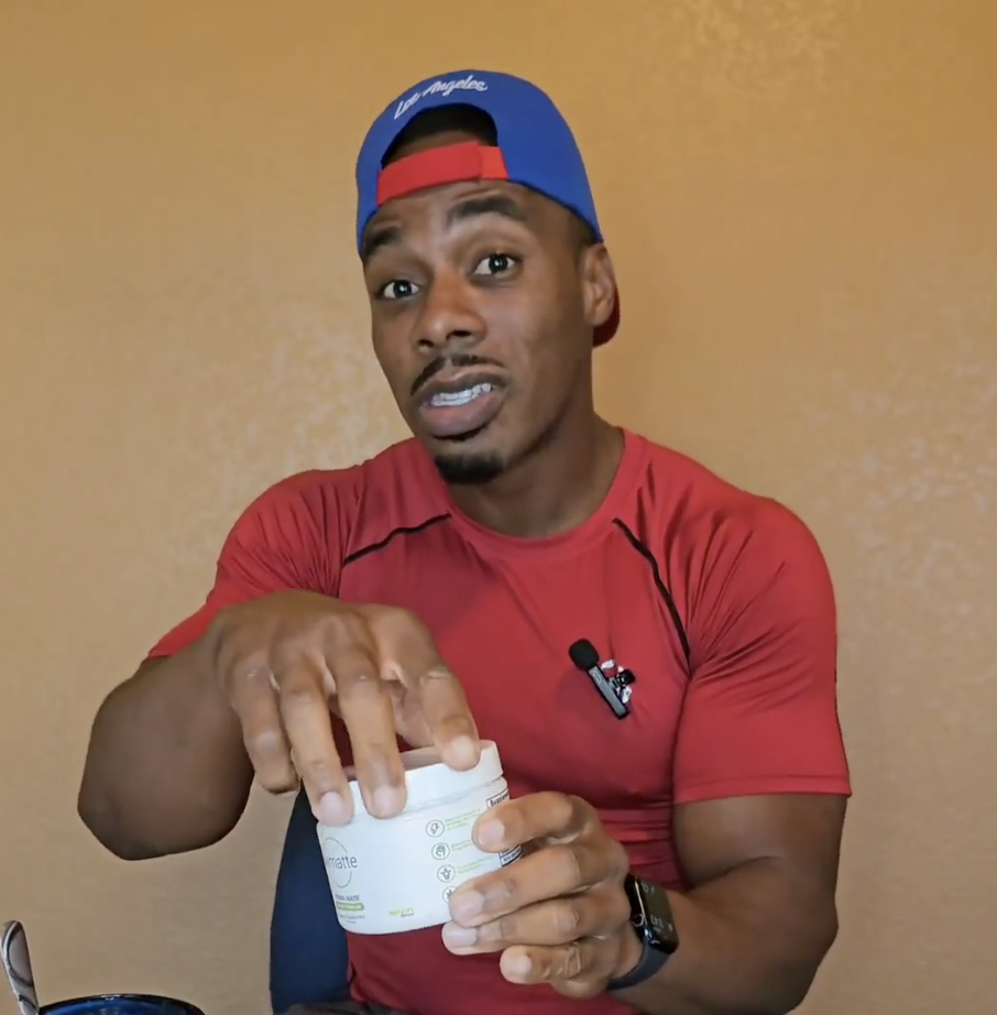 A man in a red shirt and a blue and red cap is opening a white jar.