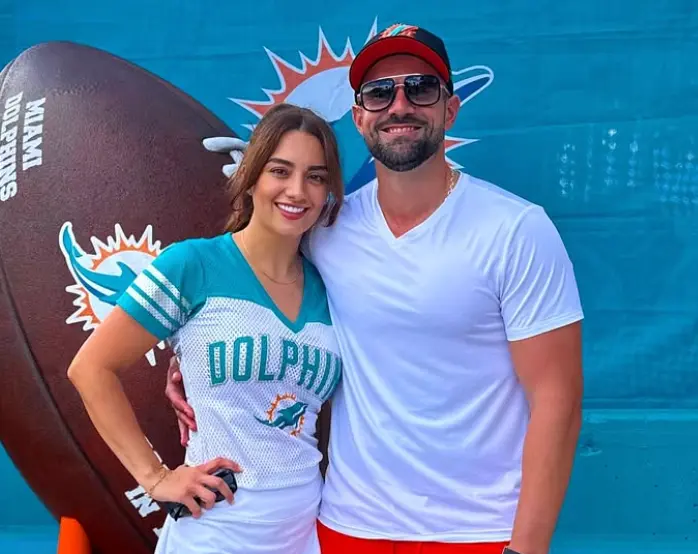 Two people posing in front of a Miami Dolphins backdrop.