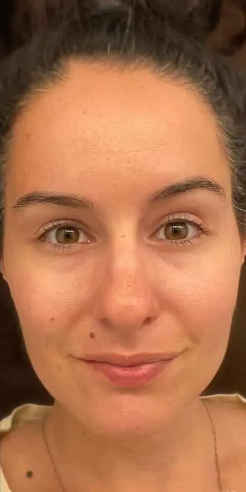 A close-up portrait of a person with a subtle smile and hair tied up.