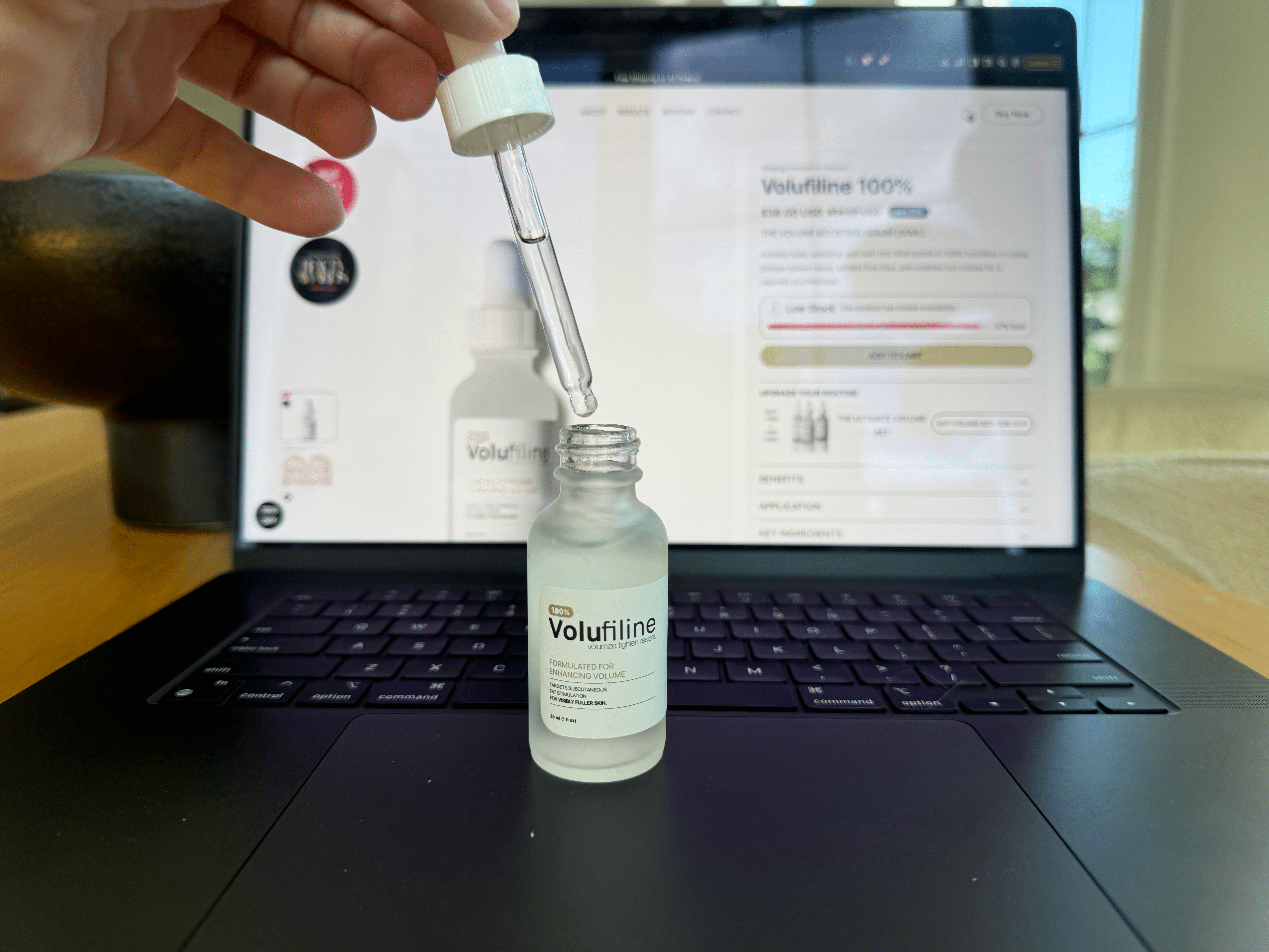 A hand holding a dropper above a Volufiline bottle in front of a laptop screen.