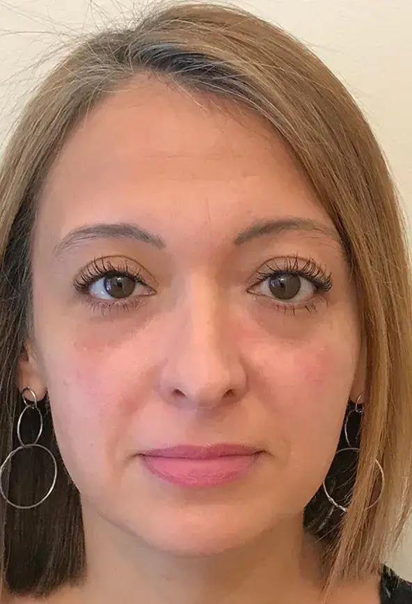 A woman with light brown hair and hoop earrings, facing forward.
