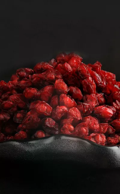 A close-up shot of a heaping pile of dried cranberries in a dark bowl against a black background.