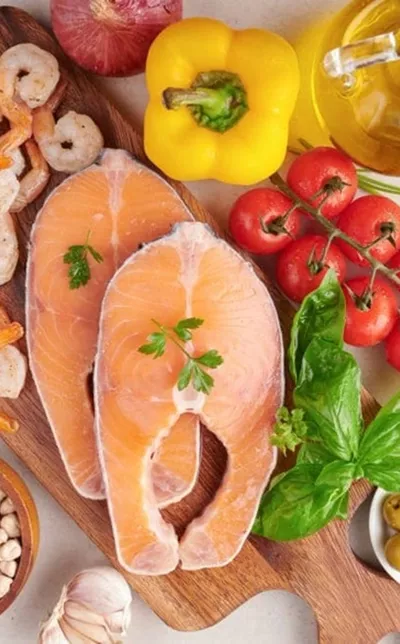 An overhead view of raw salmon steaks, shrimp, and fresh vegetables on a wooden cutting board.