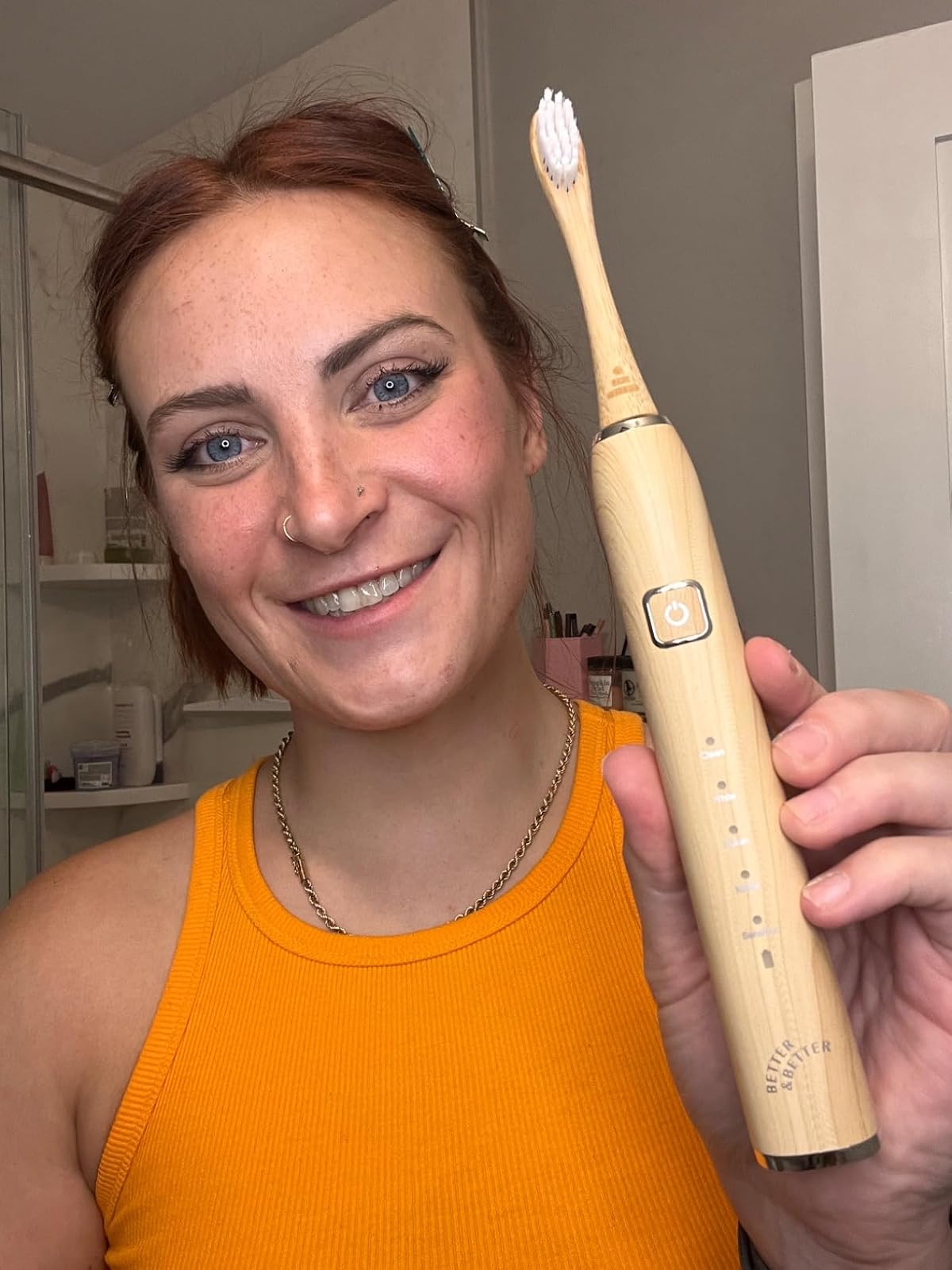 Person smiling and holding a wooden electric toothbrush in a bathroom.