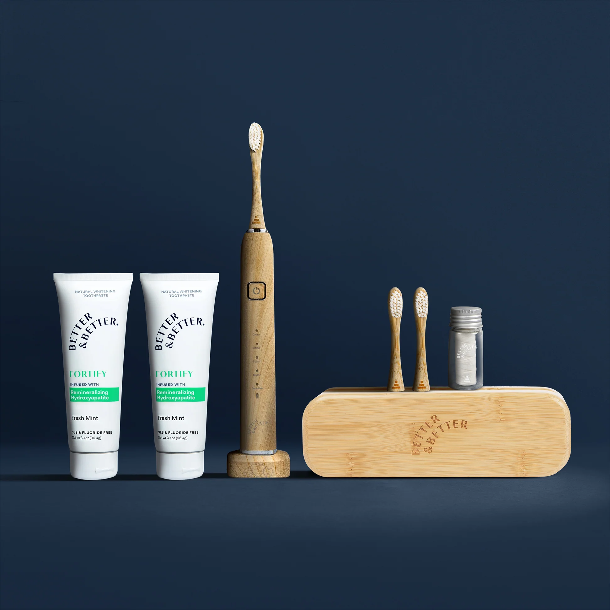 Toothpaste tubes, electric toothbrush, bamboo case, and toothbrush heads on a dark background.