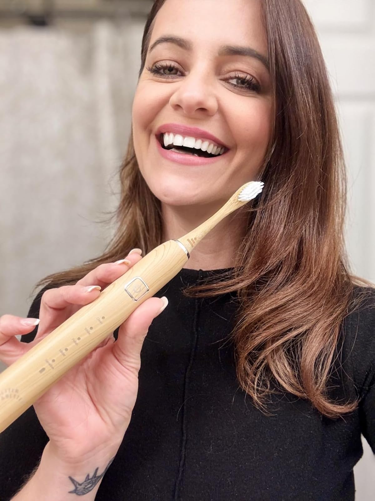 Person smiling while holding a bamboo electric toothbrush.