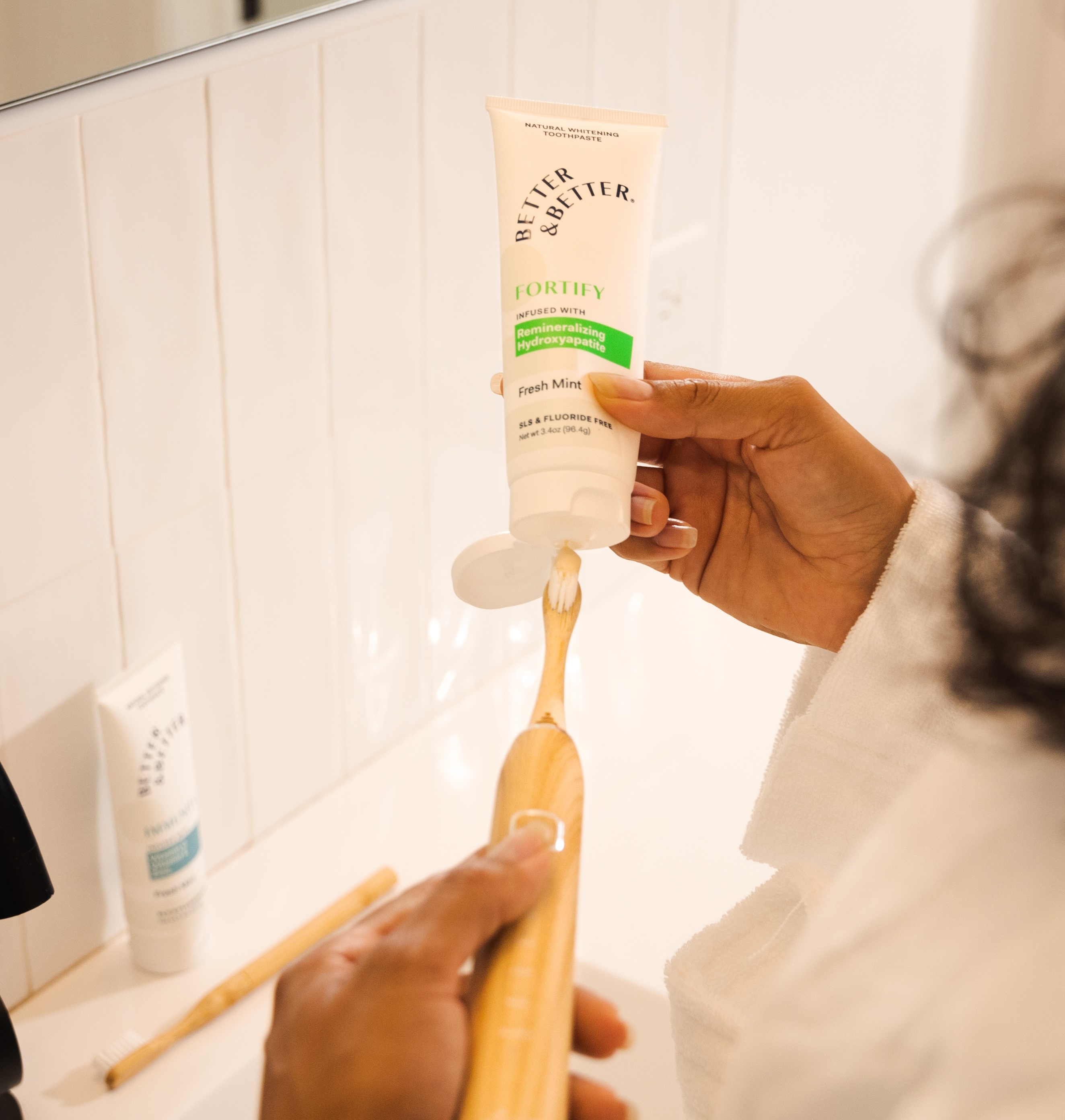 Person applying toothpaste to a bamboo toothbrush in a bathroom.