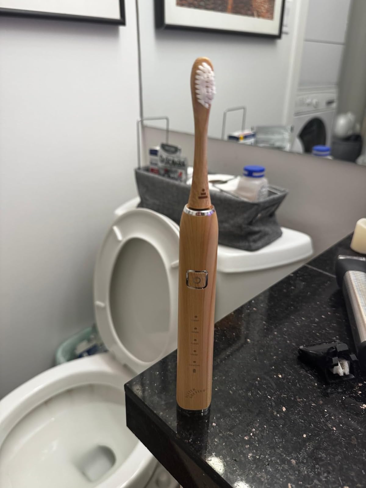 Electric toothbrush on a bathroom counter near a toilet.