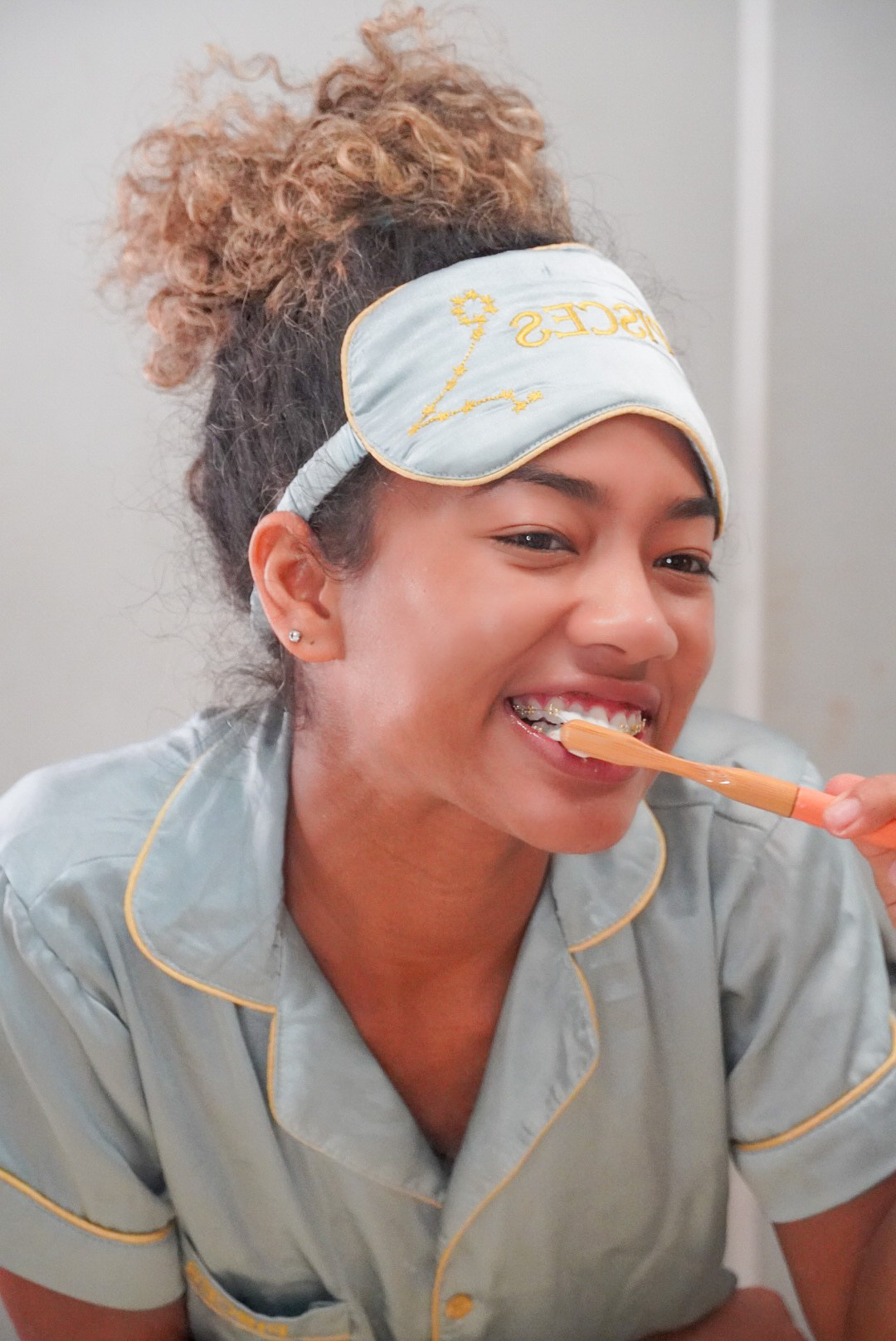Person in pajamas brushing teeth with a sleep mask on head.