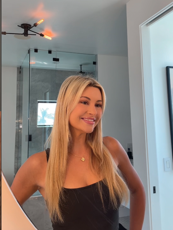 Person with long blonde hair smiling in a modern bathroom.