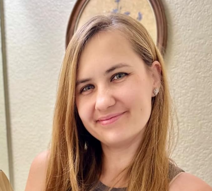 A person with long hair smiling in front of a textured wall.