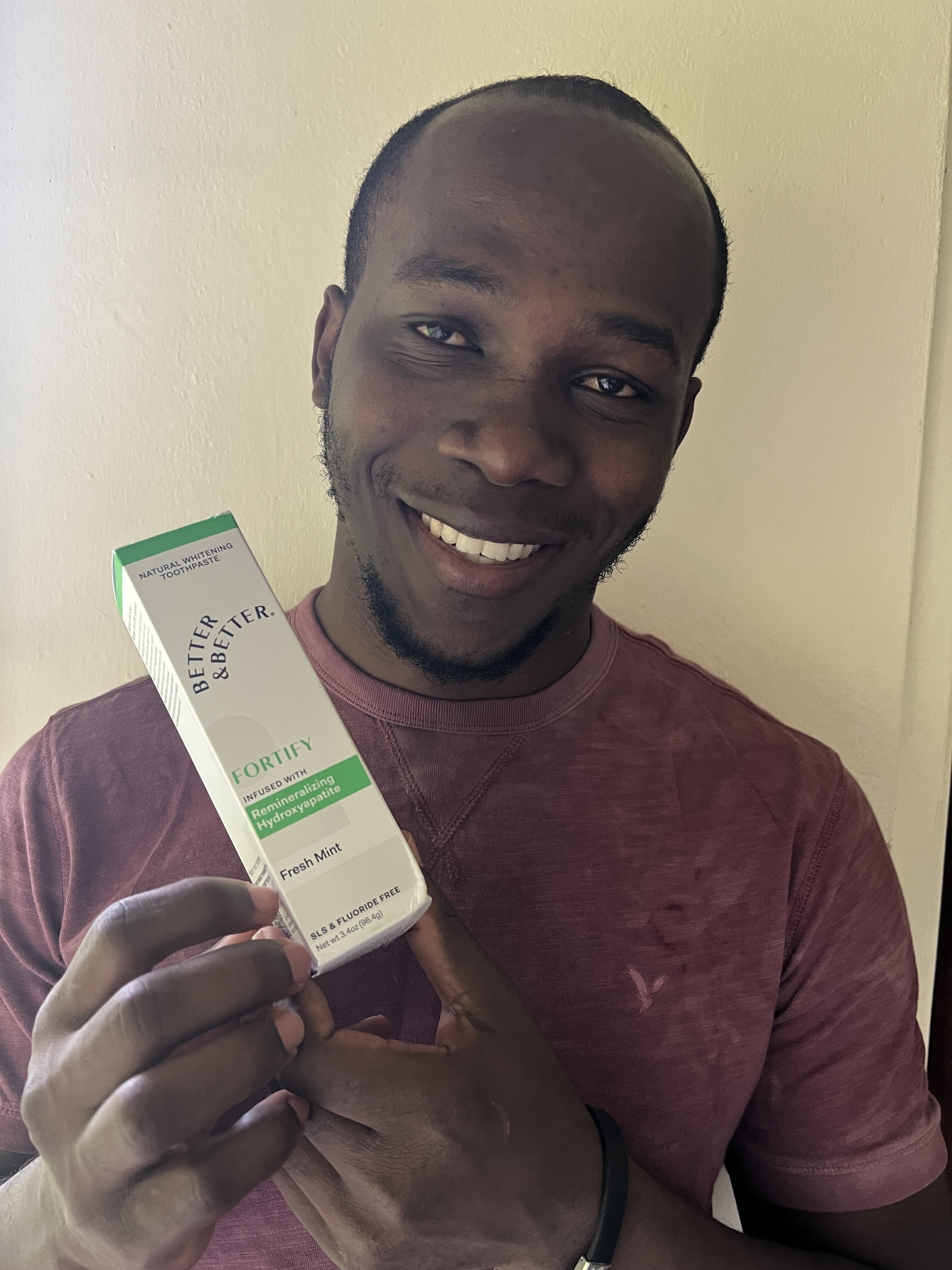 Person smiling and holding a box of toothpaste.