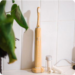 Bamboo electric toothbrush on a bathroom counter with dental floss and a plant.