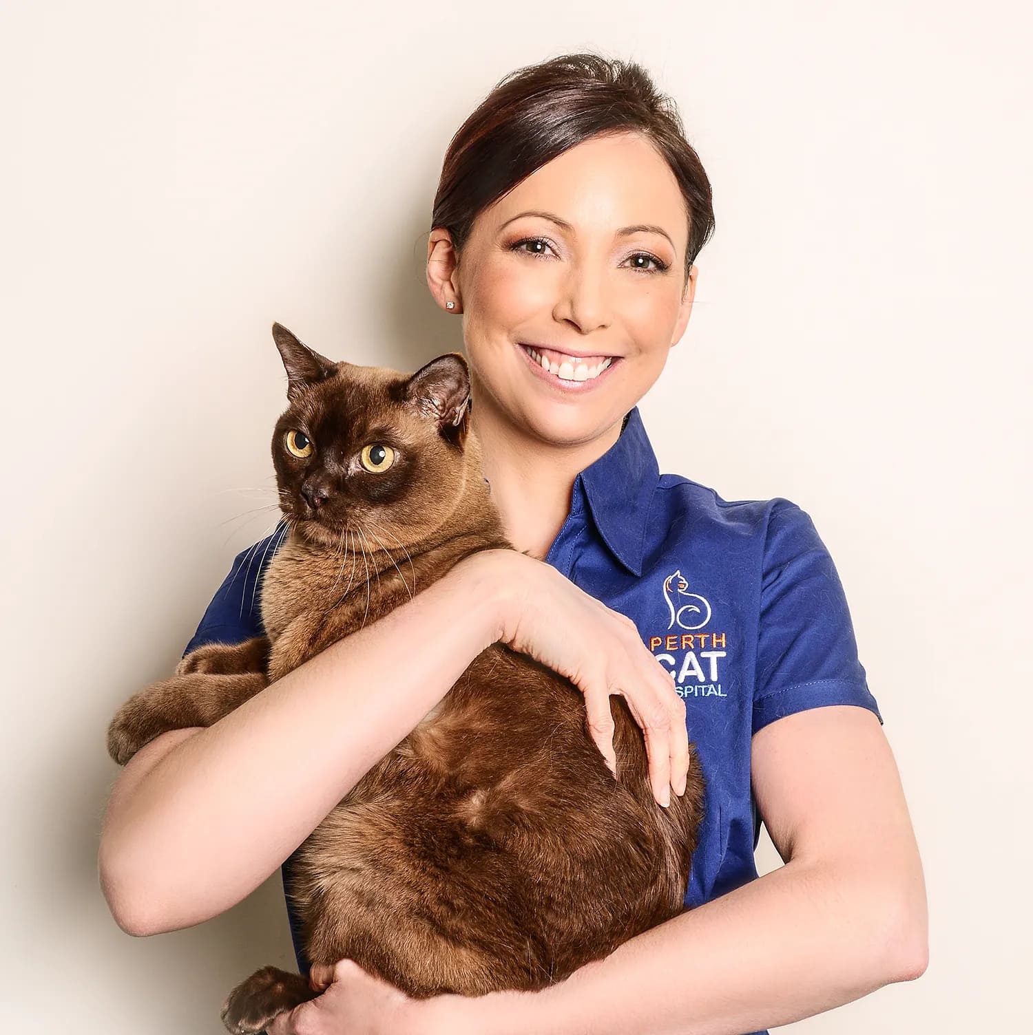 Woman in a blue shirt holding a brown cat, both smiling at the camera.