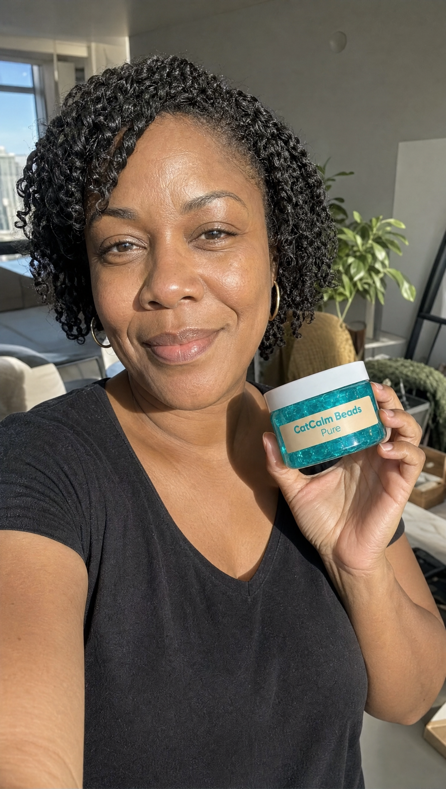 A smiling woman in a black v-neck shirt holds up a jar of CatCalm Beads Pure.