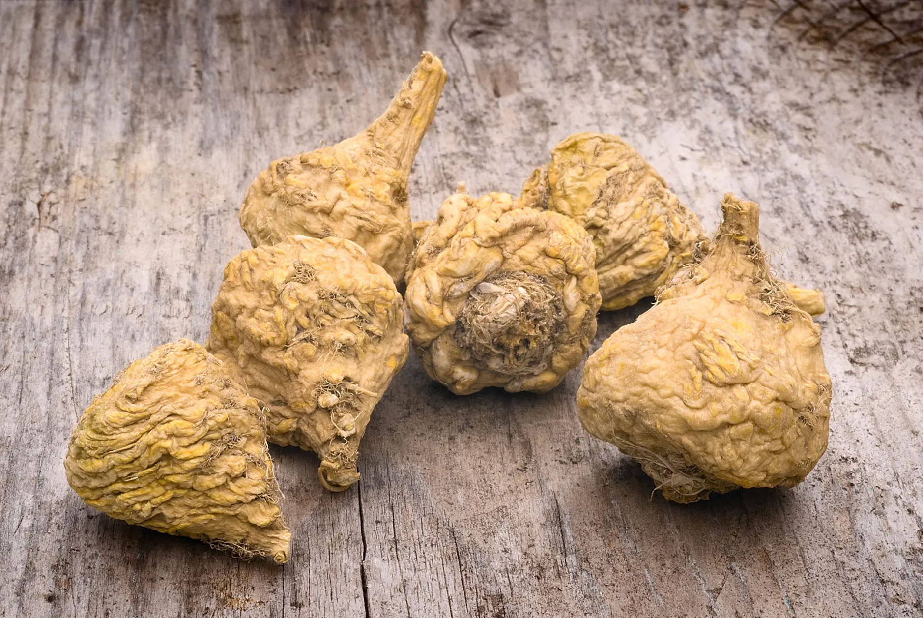 A close-up of several raw, whole maca roots sitting on a rustic, weathered wooden surface.