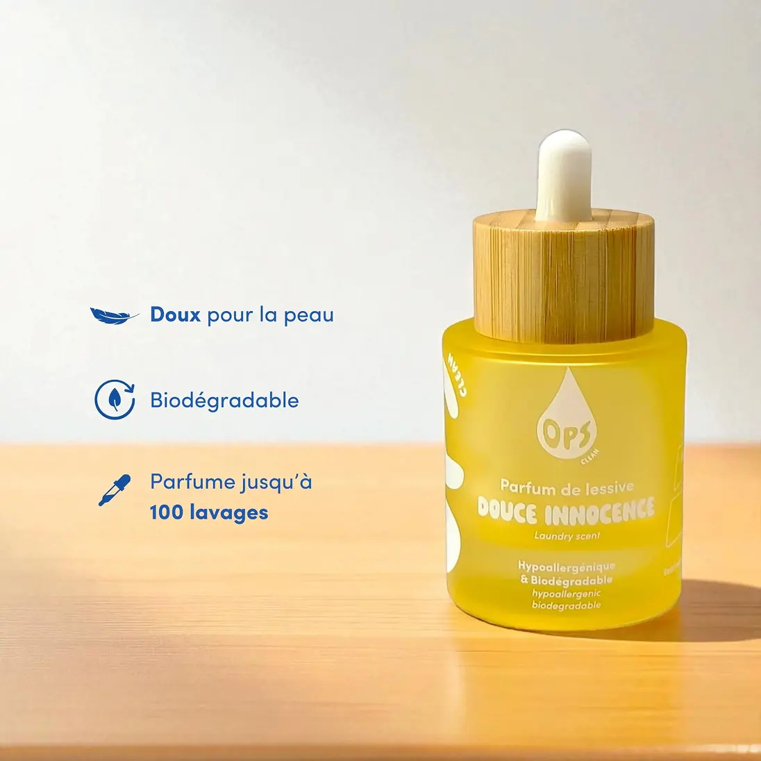 A yellow bottle of OPS laundry scent with a wooden dropper cap sits on a wooden surface.