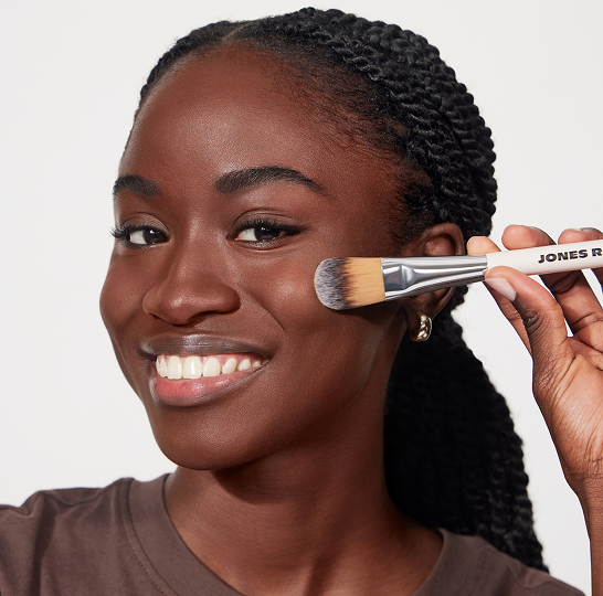Smiling person holding a makeup brush to their cheek.