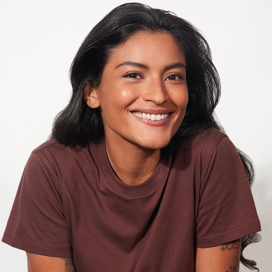 Smiling person with long dark hair wearing a brown shirt.