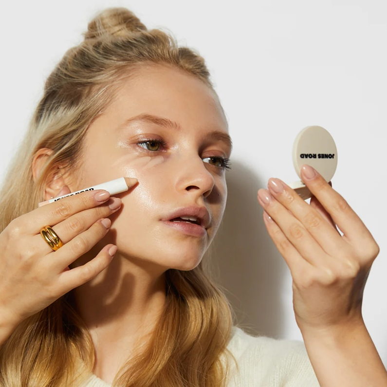 Person applying makeup with a white crayon and hand mirror.