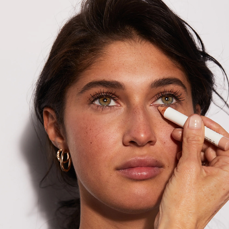 A person applies a light-colored pencil under their eye.