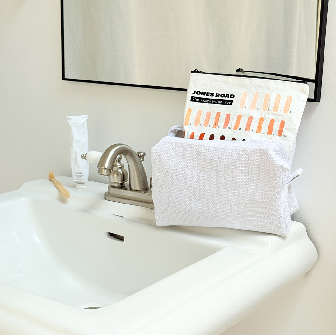Bathroom sink with a white toiletry bag and a makeup set.