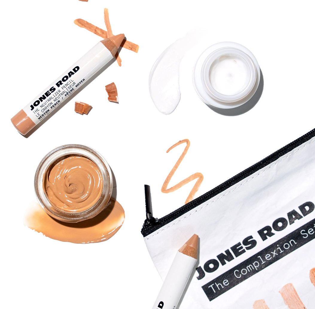 Makeup products including pencils, cream jars, and a branded pouch on a white background.
