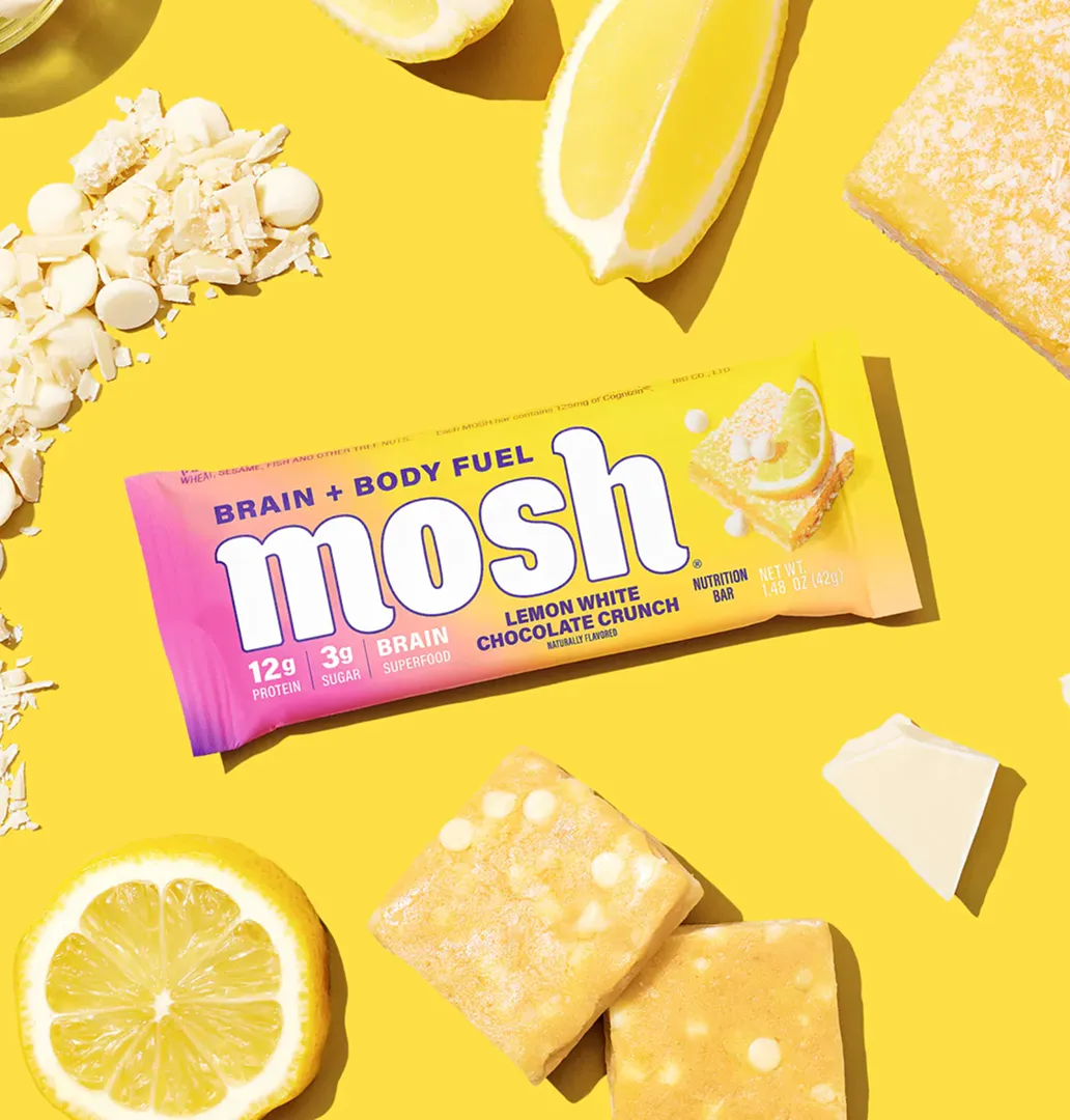A Mosh Lemon White Chocolate Crunch bar with lemons and white chocolate on a bright yellow background.
