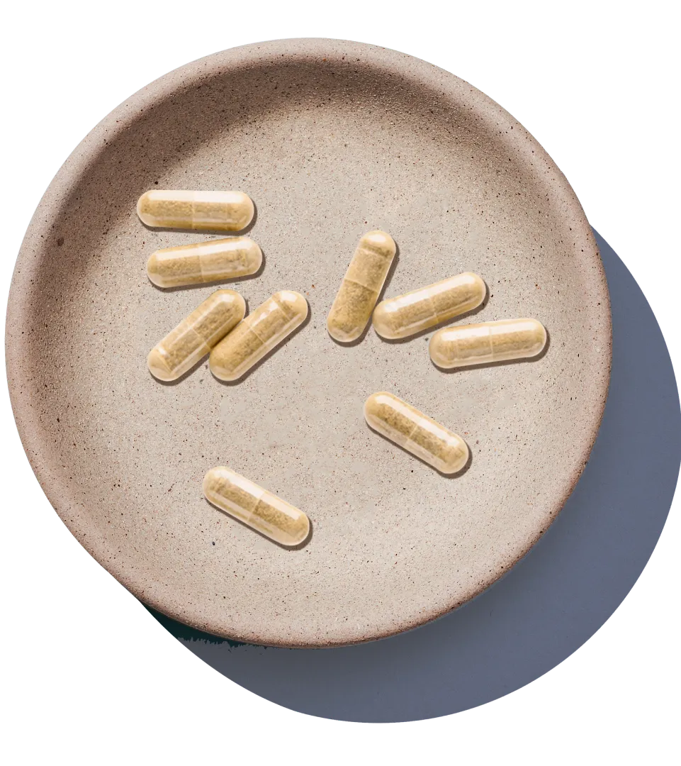 An overhead view of several beige capsules scattered in a shallow, round, stone-like dish on a white background.