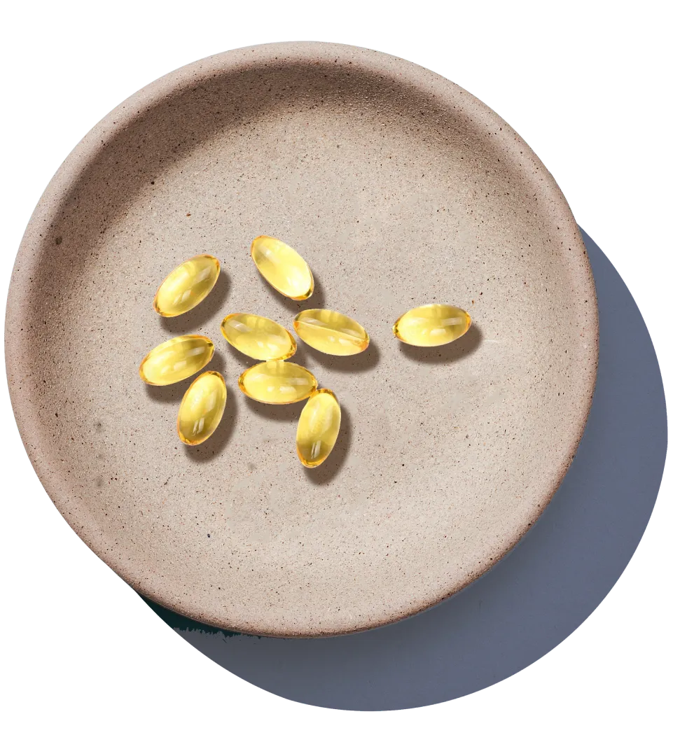 An overhead shot of several yellow softgel capsules in a shallow, textured, light-brown dish.