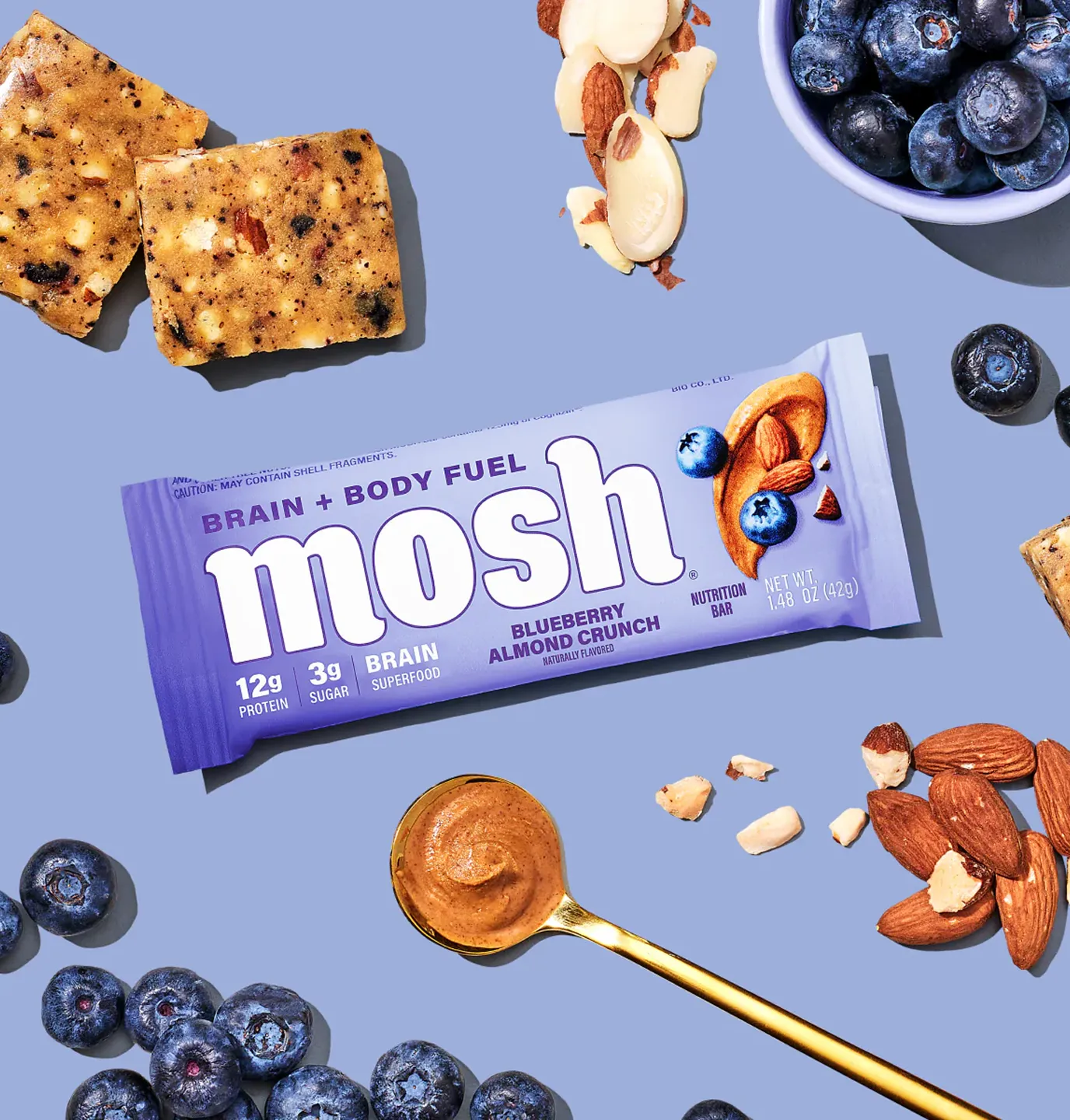 A Mosh Blueberry Almond Crunch protein bar laid flat with its ingredients: blueberries, almonds, and almond butter.