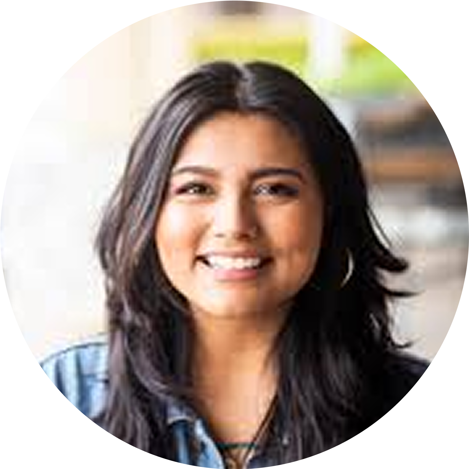 Smiling person with long hair wearing a denim shirt, blurred background.